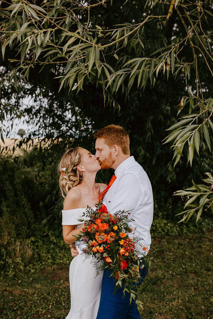 Newlyweds kissing with orange florals and botanicals
