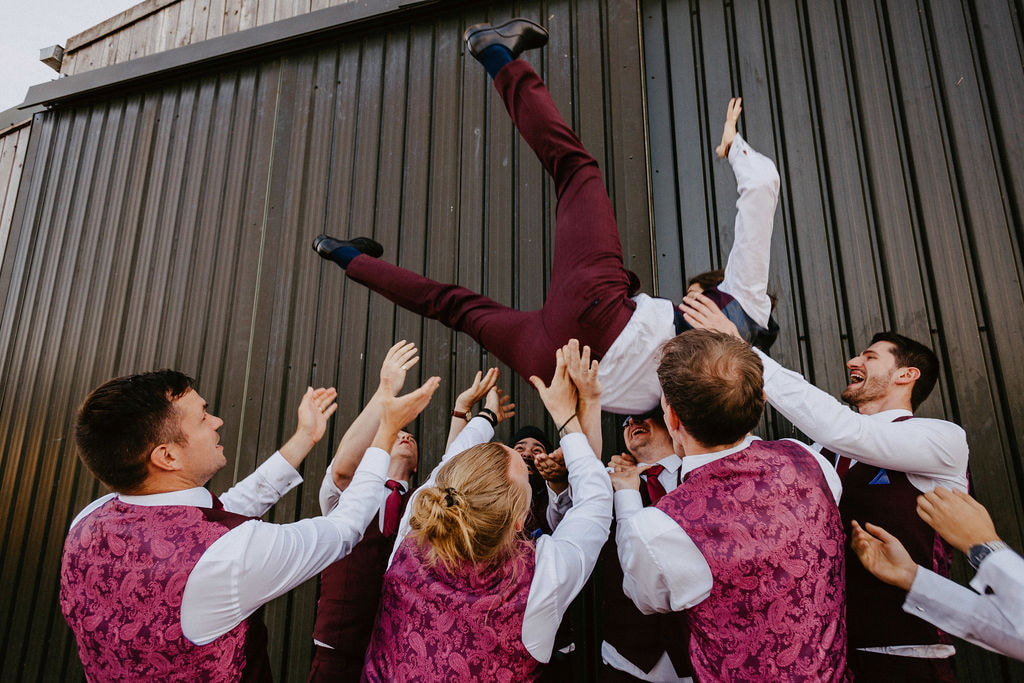 Groom being thrown in the air at wedding by groomsmen